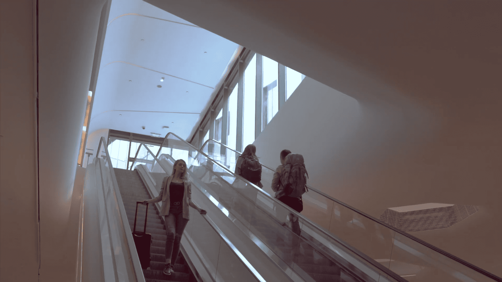 Guests on an escalator in a bright contemporary transit hall — multimedia preview still